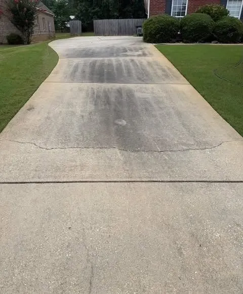 Before cleaning. Long concrete driveway with a dark center lane, then cleaned